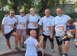 Gruppenbild beim DAK Firmenlauf: Fünf Läuferinnen und Läufer der faw stehen um einen Läufer in der Hoche, der mit dem Rücken zur Kamerau mit beiden Daumen über seine Schultern auf das faw-Logo zeigt. Der Läufer ganz rechts hat ein kind im Arm.