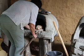 Foto wie frisch gebackenes Brot aus dem Lehmbackofen geholt wird