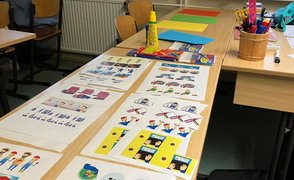 Fotografiert wurde ein Tisch, auf dem verschiedene Bastelutensilien wie Kleber, farbiges Papier und kleine ausgedruckte Illustrationen liegen.