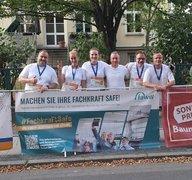 Gruppenbild: Alle sechs Läuferinnen u. Läufer stehen mit Medaille um den Hals lachend hinter einer Absperrung, an der ein Werbebanner der faw angebracht ist: Aufschrift: Machen Sie Ihre Fachkraft safe!