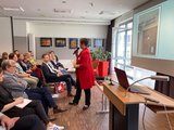 Eva Ullmann vom Deutschen Institut für Humor Galeriebild: Frau mit Mikrofon spricht mit den Besucher*innen der Tagung.