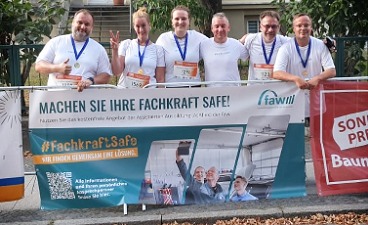 Gruppenbild: Läuferinnen und Läufer der faw mit Medaille stehen hinter einem faw-Werbebanner an einer Absperrung des DAK Firmenlaufs.