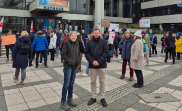 Zwei Mitarbeitende der faw stehen mit anderen Teilnehmenden der Kundgebung auf einem Platz vor dem Offenbacher Rathaus.