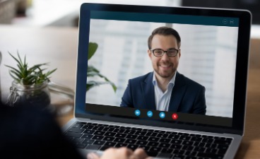 Symbolbild eines Online-Vorstellungsgespräches: Vom geöffneten Laptop blickt ein Mann lächelnd auf die Person am Laptop.